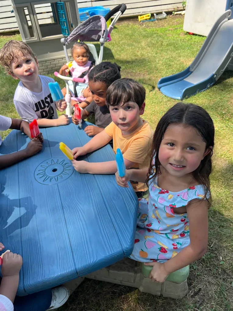 Children enjoying ice pops together at an outdoor picnic table
